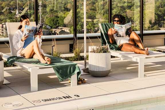 Two people are sitting on lounge chairs by a pool, reading books at Scout Living, powered by Placemakr, Atlanta,30308
