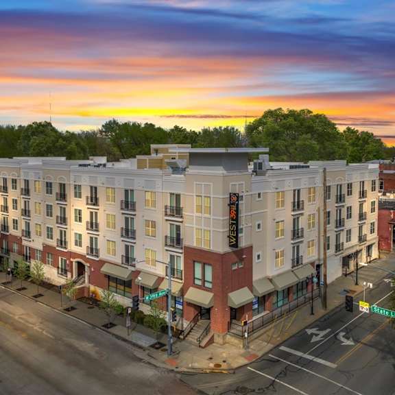 A sunset view of a street with a multi-story building on the corner.
