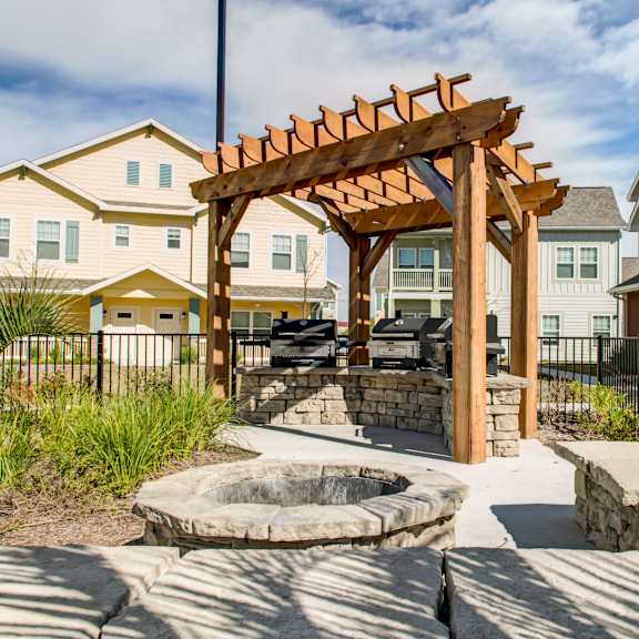 A wooden pergola is in the middle of a courtyard with a fire pit.