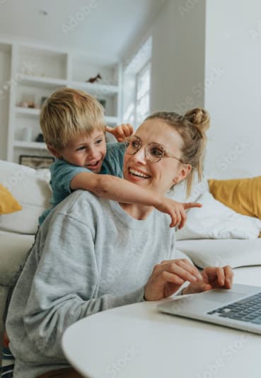 a woman working on a laptop computer with a young boy sitting on her back at King Arthurs Court, Washington
