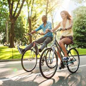 Two people riding bicycles on a sunny day in a park.