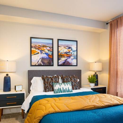 A bedroom with a bed, two lamps, and two pictures on the wall.