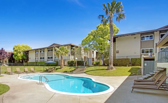 a swimming pool with chaise lounge chairs and trees in the background