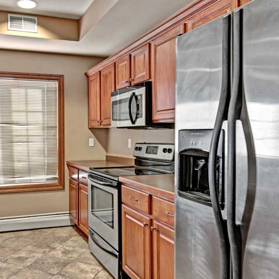 A kitchen with stainless steel appliances, light countertops, and wooden cabinets at Grand River Estates. 