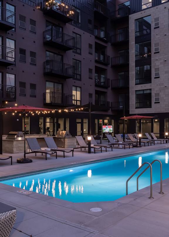 A swimming pool surrounded by lounge chairs and umbrellas in a courtyard.
