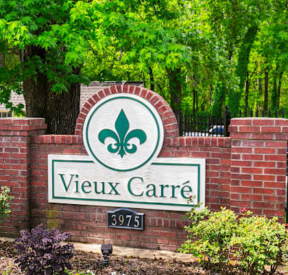 A sign that says Vieux Carre in front of a fence.