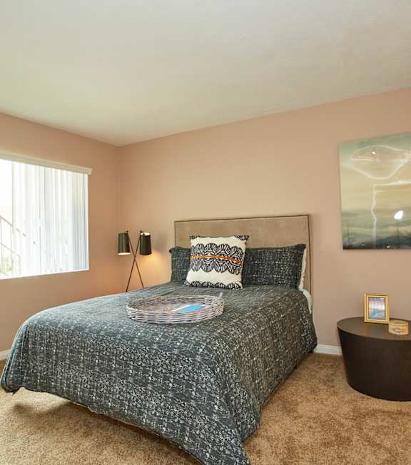 A bedroom with a bed, a side table, and a painting on the wall.