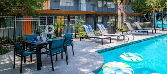 Community pool at fifteen 50 apartments in Las Vegas, NV, 89119 with lounge chairs and patio umbrellas