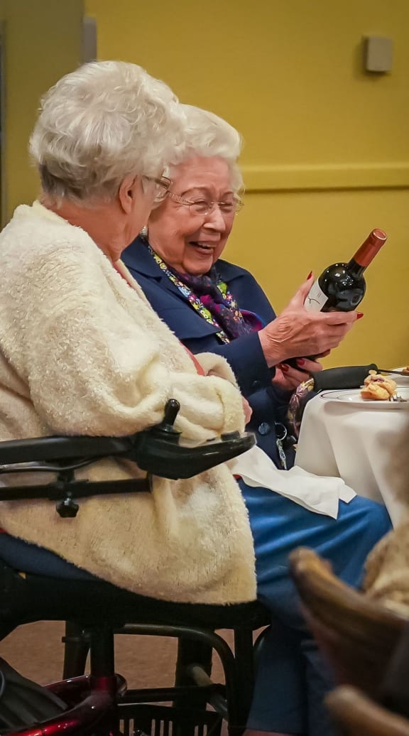 two elderly women sitting at a table with a bottle of wine at Winding Commons Senior Living, Carmichael