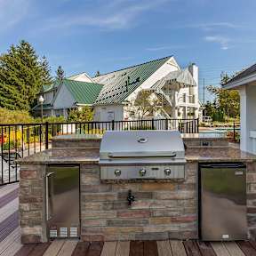 A stone outdoor kitchen with a grill and two trash bins.