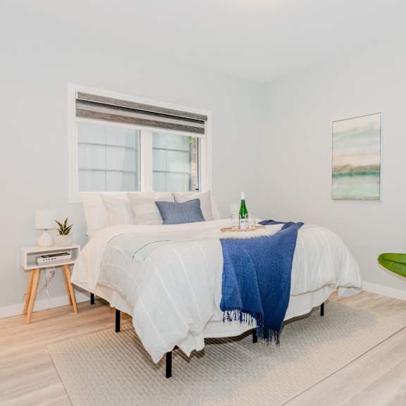 A bedroom with a large bed, a painting on the wall, and a wooden floor.