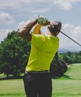 A man in a yellow shirt is swinging a golf club on a golf course.