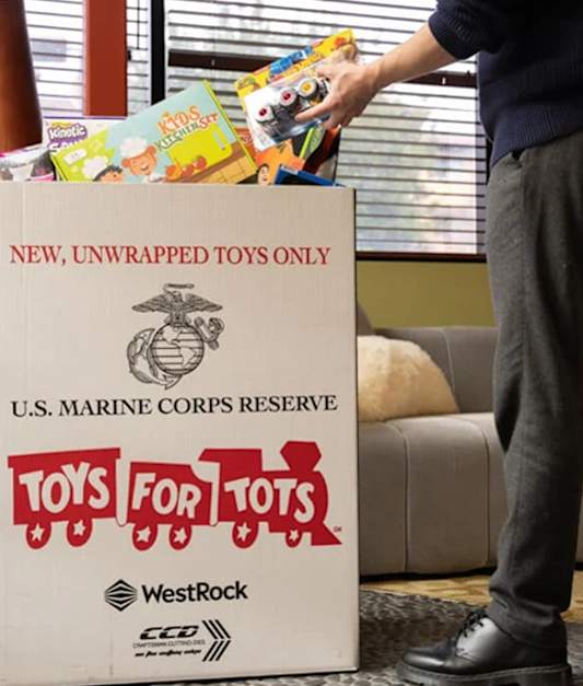 A man is handing over a box of unwrapped toys to the U.S. Marine Corps Reserve Toys for Tots program.