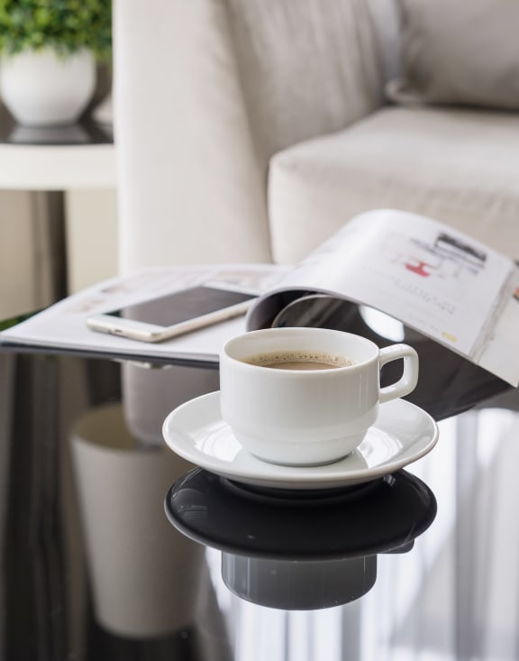 Cup of coffee, magazine, and phone on a coffee table in a living room
