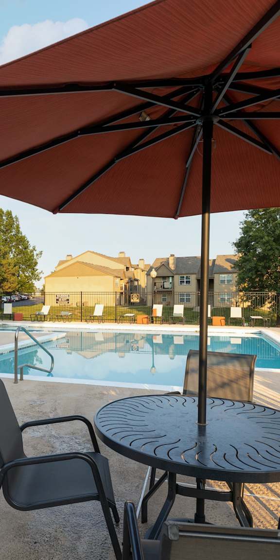 Patio with table, chairs, and umbrella overlooking the pool at The Lakes Apartments.