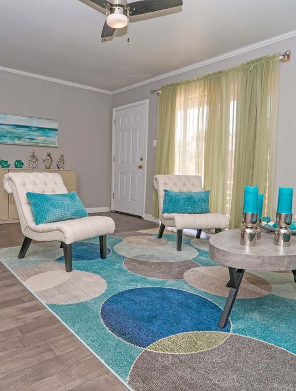 A cypress living room with a blue and white rug, a white chair, and a painting of a beach scene on the wall at The Marq in Shreveport, LA