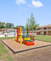 A playground with a slide and a sandbox in the middle of a grassy area.
