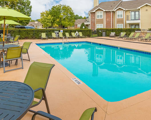A pool surrounded by chairs and umbrellas with a building in the background. at Central on the Green Apartment Homes, North Carolina, 27604