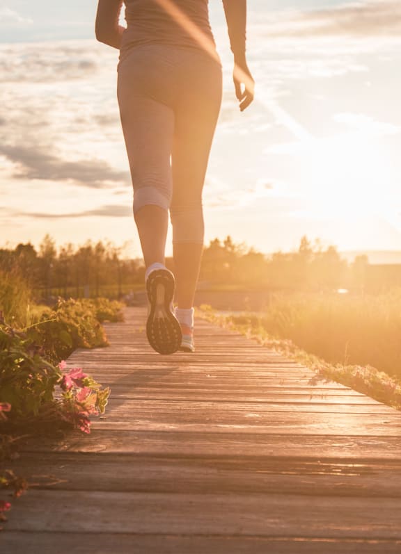 a woman walking on a wooden pathway at sunset