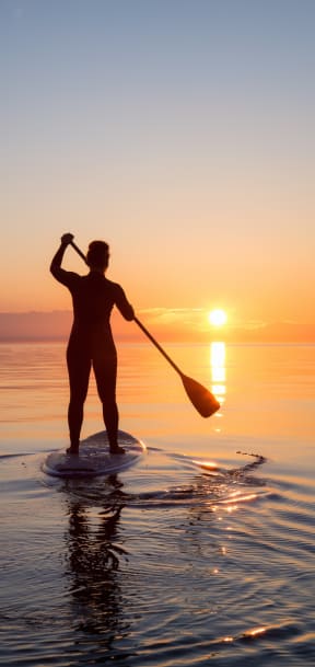 Woman Paddle Boarding During Sunset
