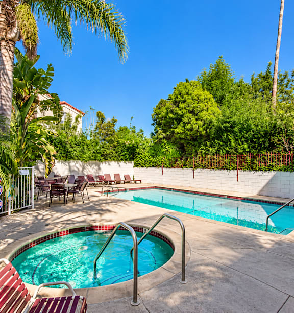 A pool surrounded by chairs and trees.