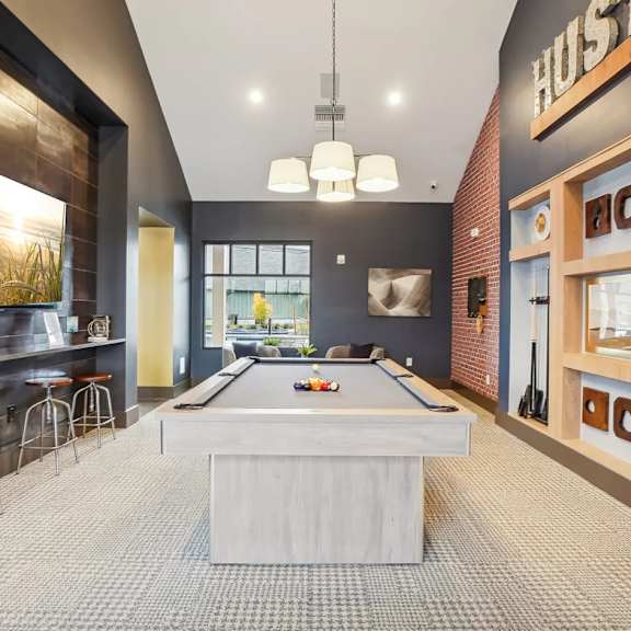 A pool table is in the middle of a room with a bar and a wall with a picture of a pool table.