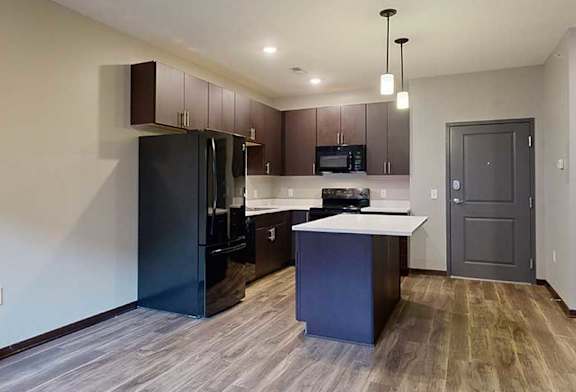 an open-concept living room and kitchen with dark cabinets and black appliances