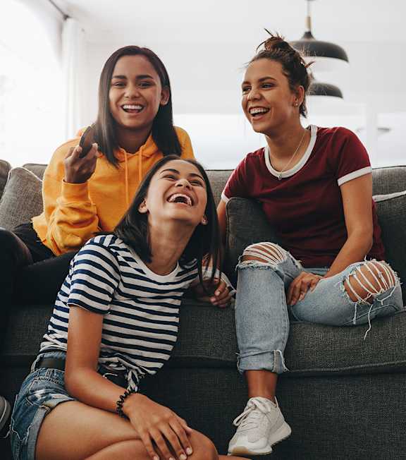 Three women are sitting on a couch, laughing and enjoying each other's company.