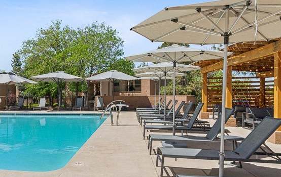 the resort style pool is surrounded by lounge chairs and umbrellas at Acacia Gardens, Albuquerque, NM, 87111