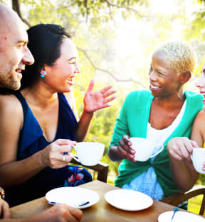 Group of 4 Friends Sitting Around Table Outside with Coffee Cups