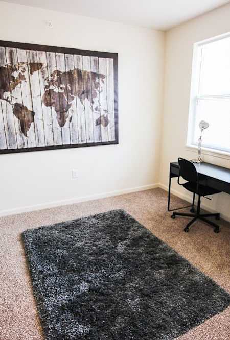 A room with a world map on the wall and a black desk with a chair.