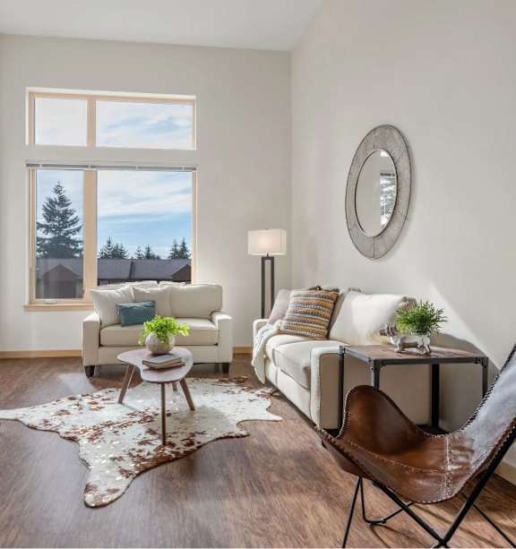 A living room with a white couch, a brown leather chair, and a rug with a cowhide pattern.