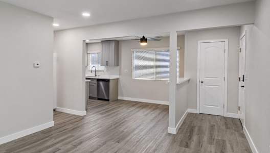 a renovated living room and kitchen with white walls and wood flooring