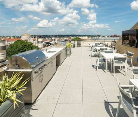 a rooftop patio with tables and chairs and a barbecue grill