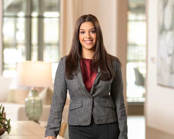 A woman in a grey suit stands in a room with a table and chairs.