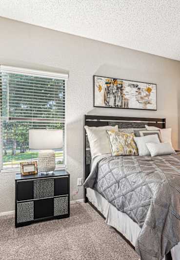 Comfortable bedroom with a grey upholstered bed and neutral decor at Laurels of Sendera apartments in Arlington, TX