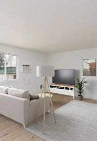 A modern living room with a white sofa, a wooden floor, and a large window.