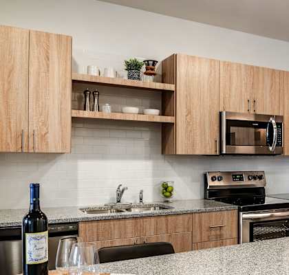 Modern apartment kitchen with light wood cabinets, granite countertops, and stainless steel appliances at Brandywine Green