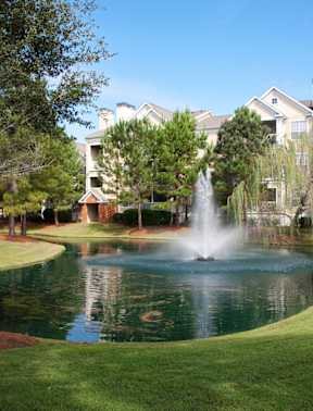 A fountain in the middle of a pond in front of a building.
