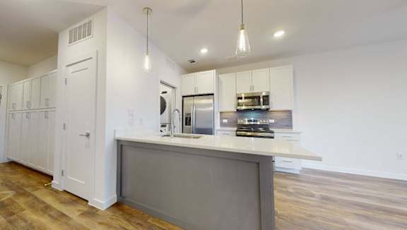 A modern kitchen with white cabinets and a wooden floor.