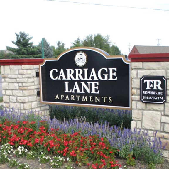 A sign for Carriage Lane Apartments is surrounded by flowers.