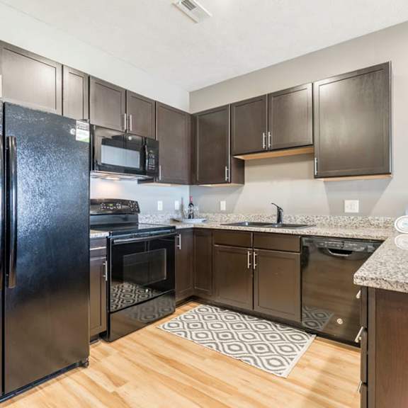A kitchen with wooden floors and a black refrigerator.