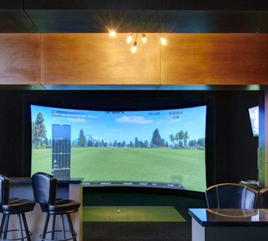 a golf simulator in a room with chairs and a bar