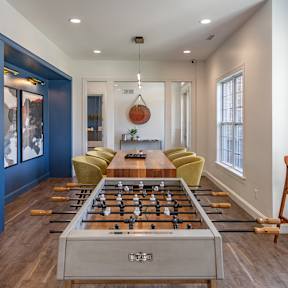 A foosball table is in the middle of a room with a blue cabinet and yellow chairs.