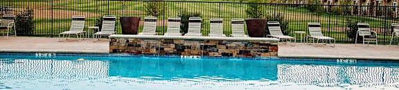 A swimming pool with sun loungers and a row of houses in the background.