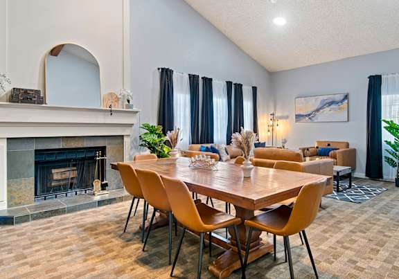 Community cabana showcasing a fireplace, wooden table, with brown leather couches and curtained  at Riverwood Apartments in Washington