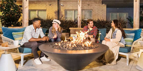 Four people sitting around a fire pit on a patio.