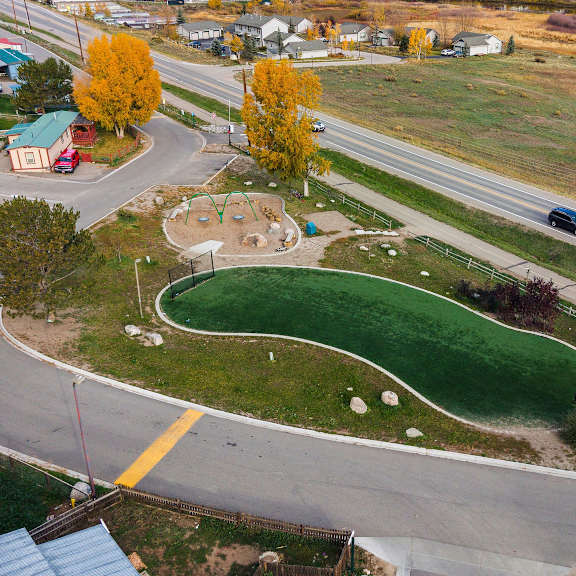 A road with a curve and a green field with a playground.
