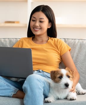 asian woman with dog on sofa reading laptop