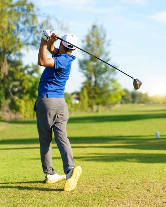 A man in a blue shirt and white cap is playing golf.